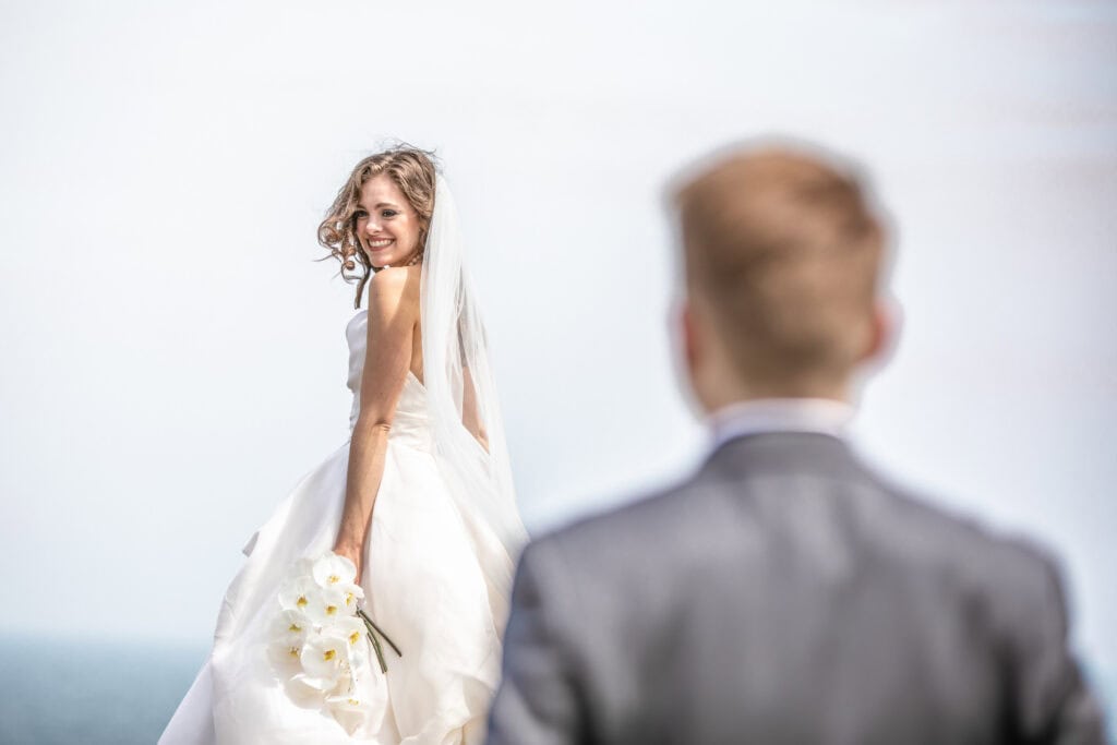 Bride smiles at groom by the sea.