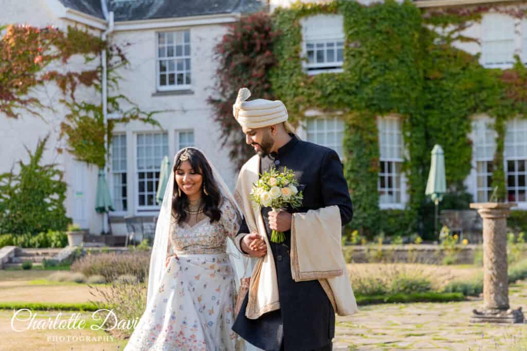 Muslim couple in their formal Nikah attire walking with bouquet in Rufflets Hotel garden, St Andrews.