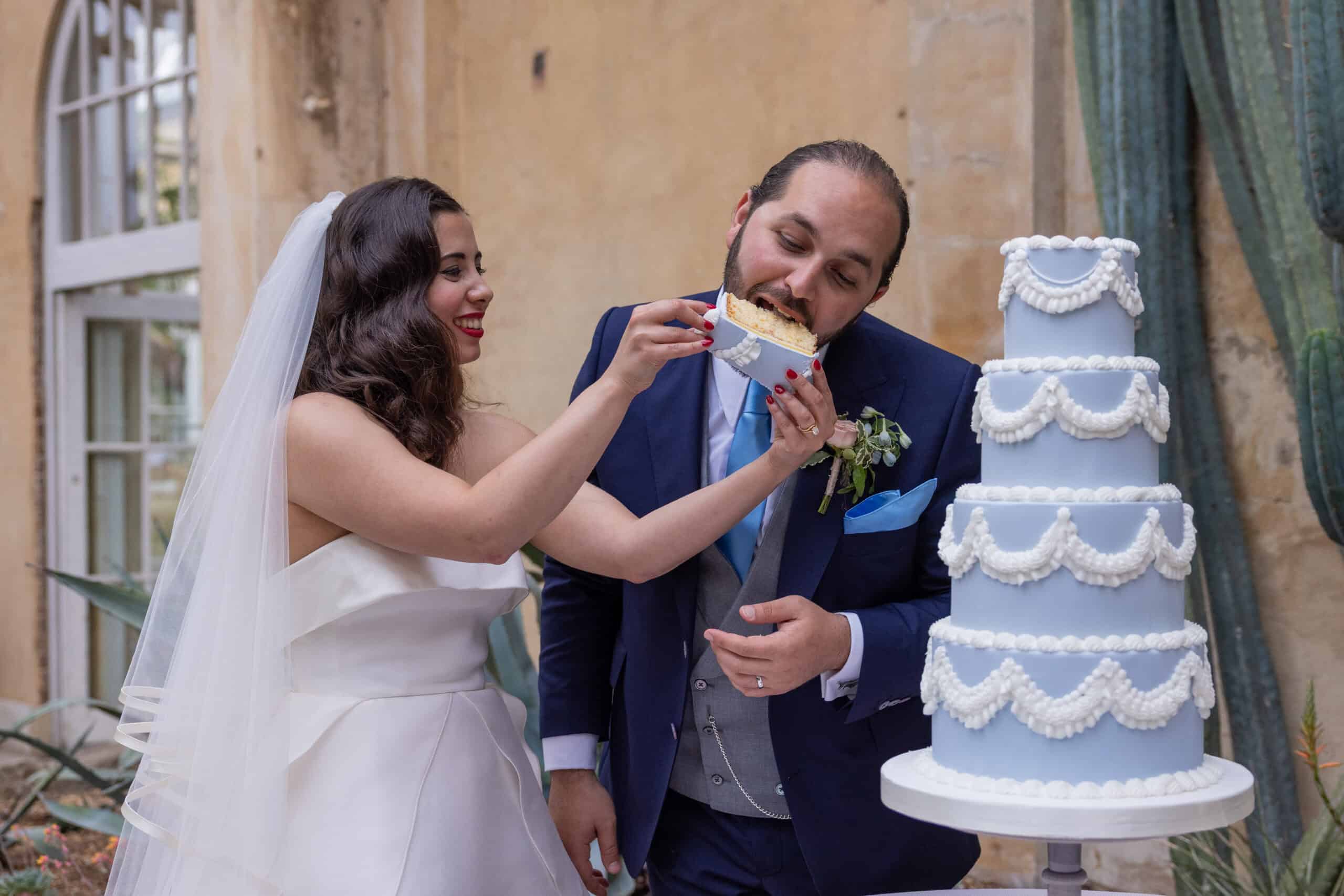 Bride feeding groom wedding cake slice and laughing.