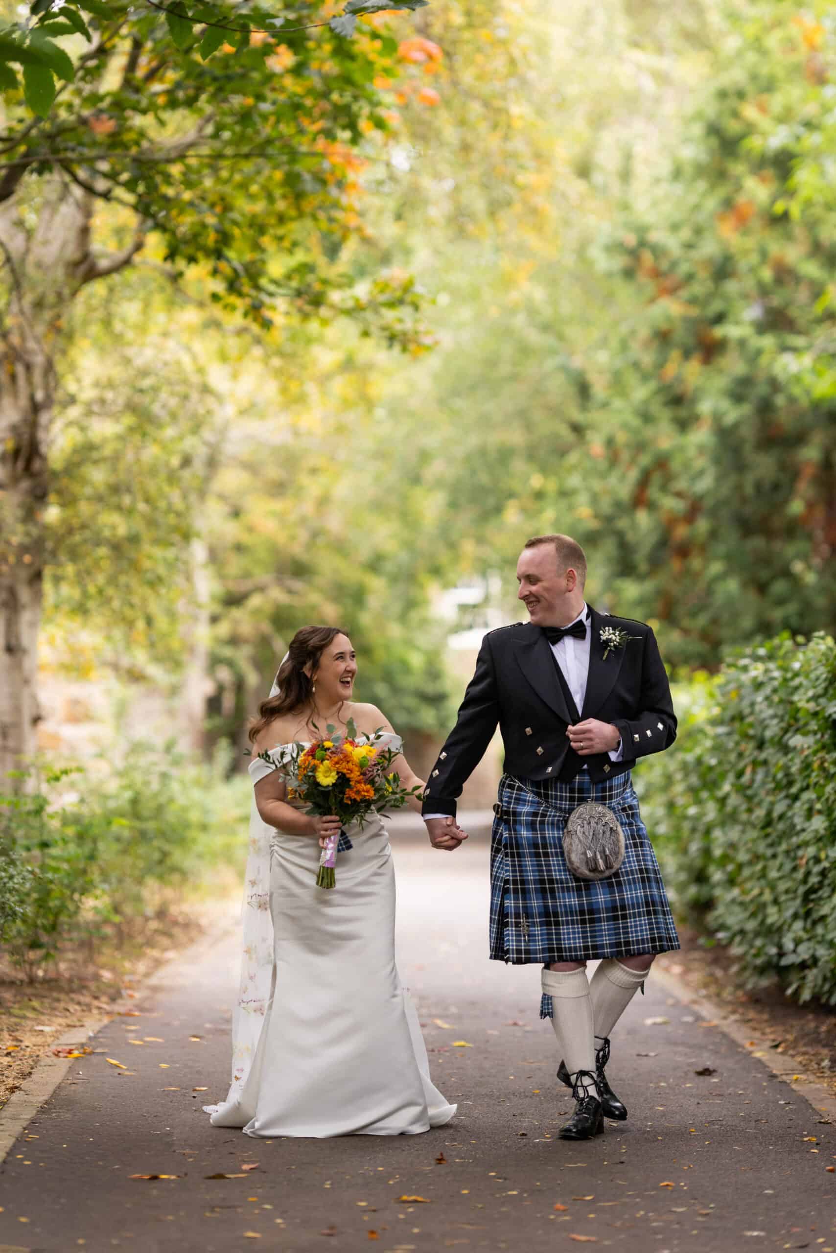 Bride and groom walking in park, holding hands.