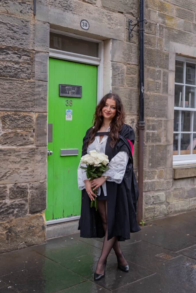Graduate holding flowers in front of green door.