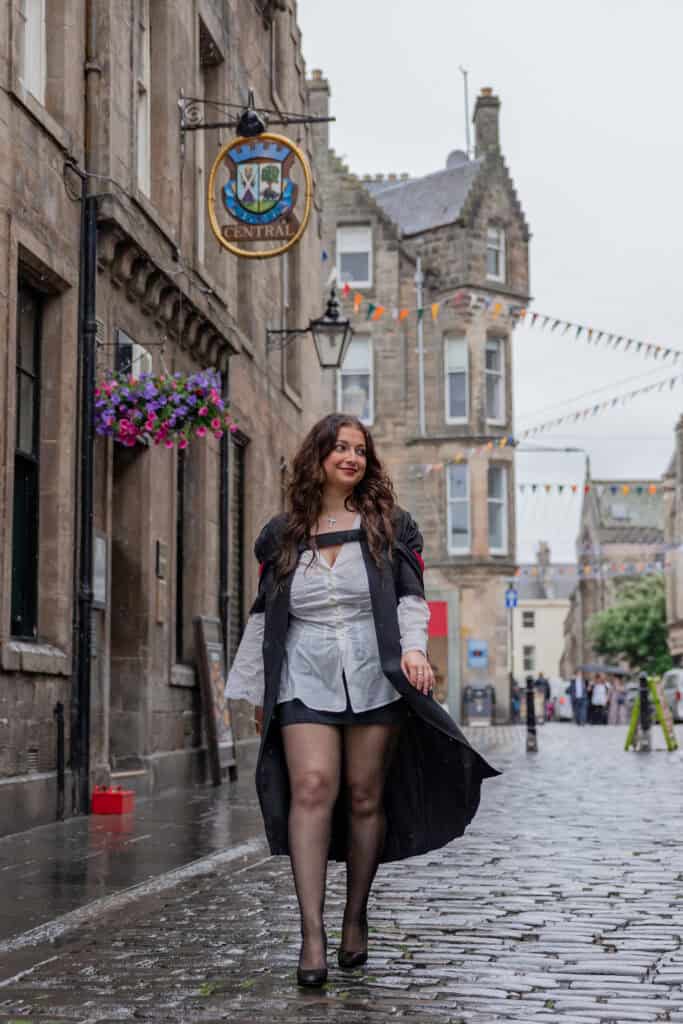 Woman walking on cobblestone street in graduation attire.