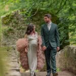 Couple walking on forest path in elegant attire.