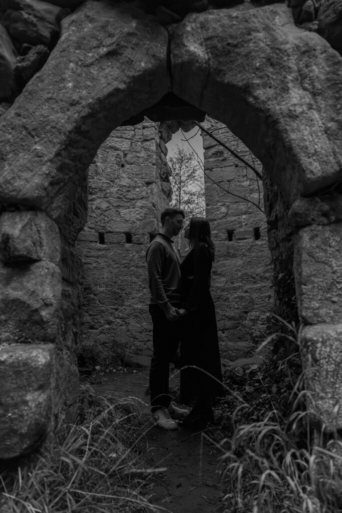 Couple standing romantically under ancient stone archway leading to historic Ice House of Dalhousie Castle.