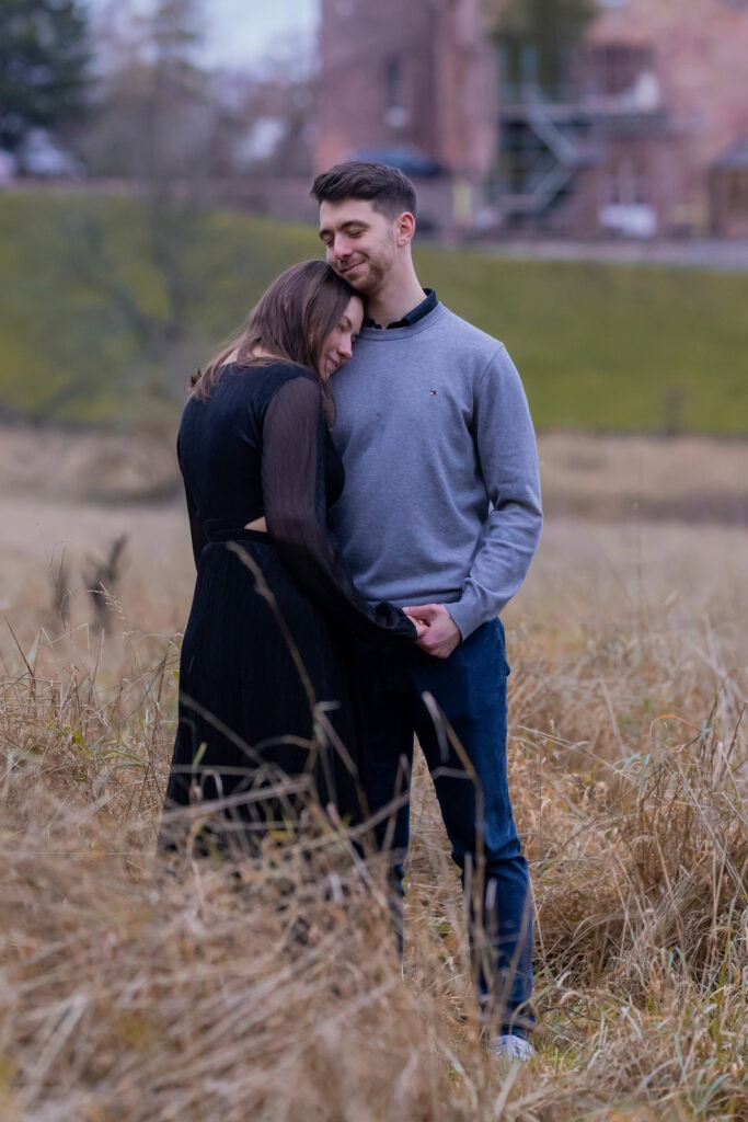 Couple embracing in grassy fields in front of Dalhousie Castle, Scotland.
