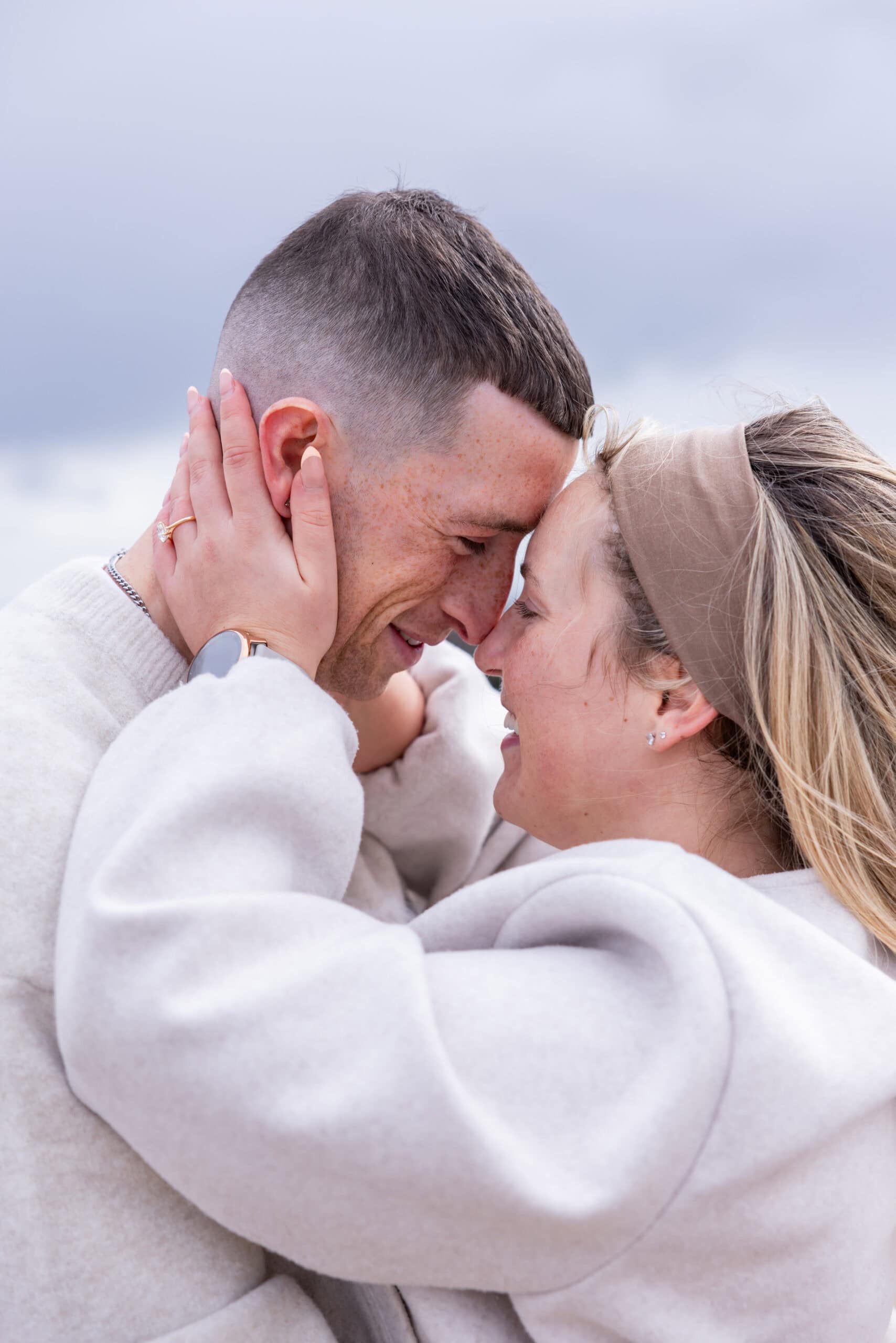 Charlotte Davies Photography - St. Andrews Wedding Photographer. A couple wearing light-coloured clothing stands close, touching foreheads and smiling at each other, with the woman holding the man's face in her hands.