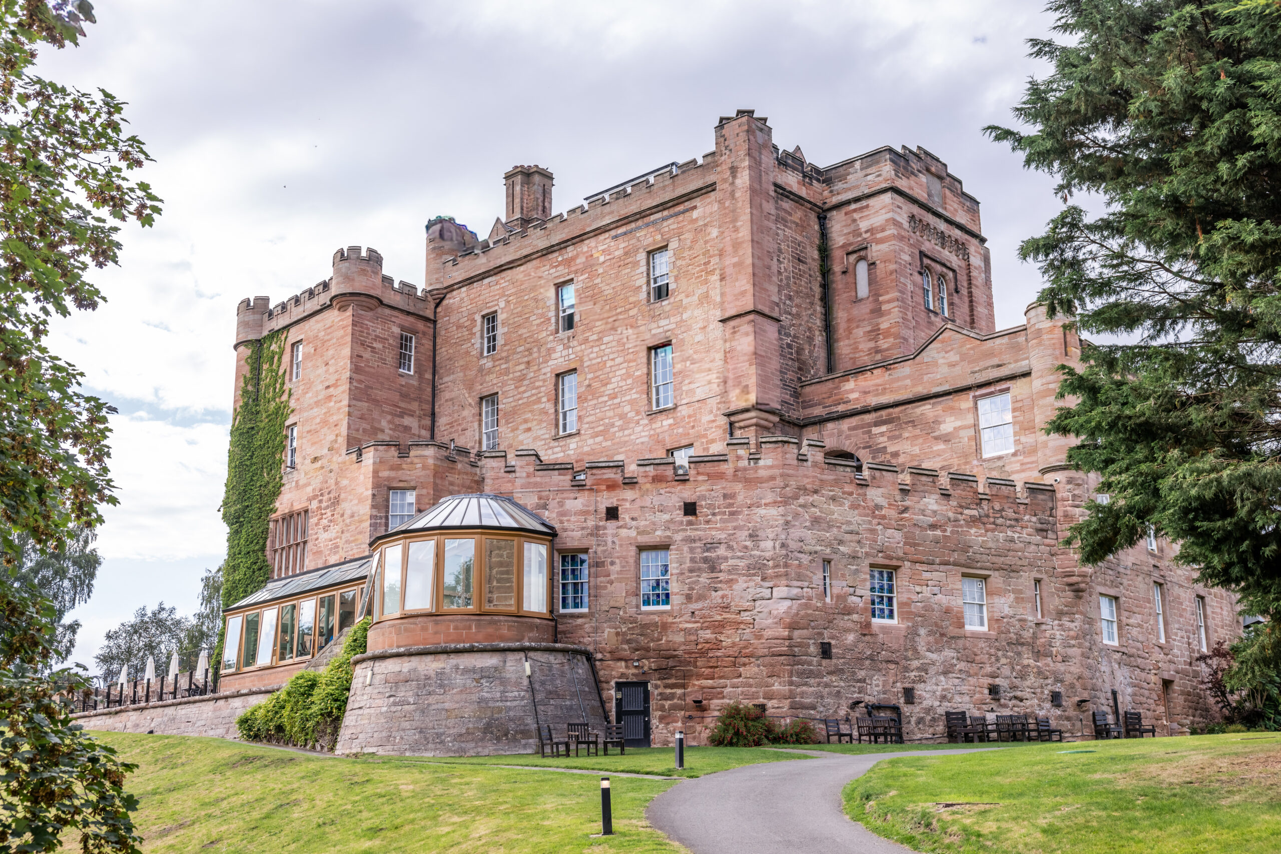 Red sandstone castle with battlements beside landscaped lawn