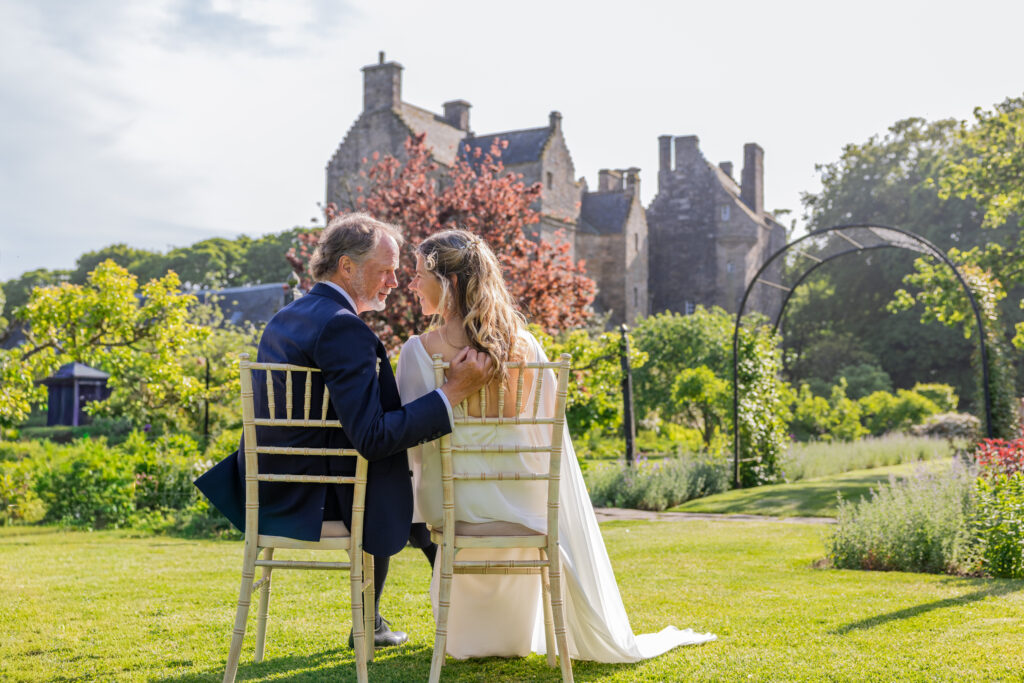 Newlyweds seated in castle garden, sharing a tender moment