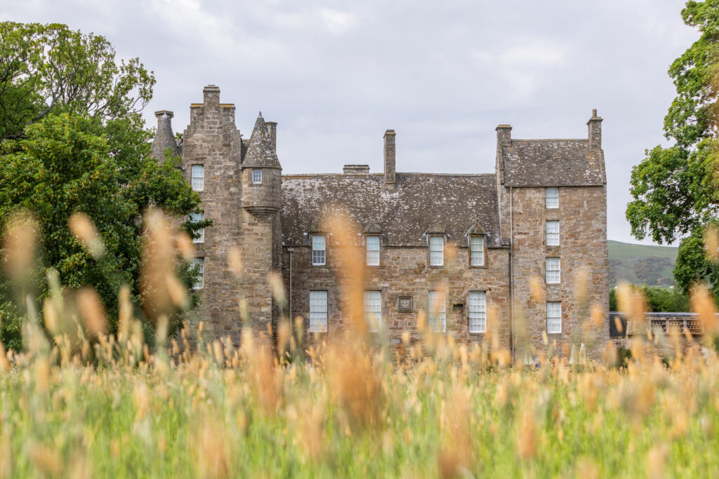 Historic Kellie Castle, Fife, framed by wild grasses and trees.