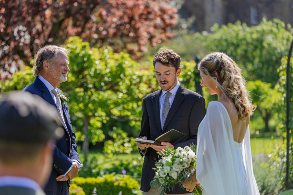 Couple exchanging vows during a sunny garden wedding ceremony at Kellie Castle, Fife, Scotland.