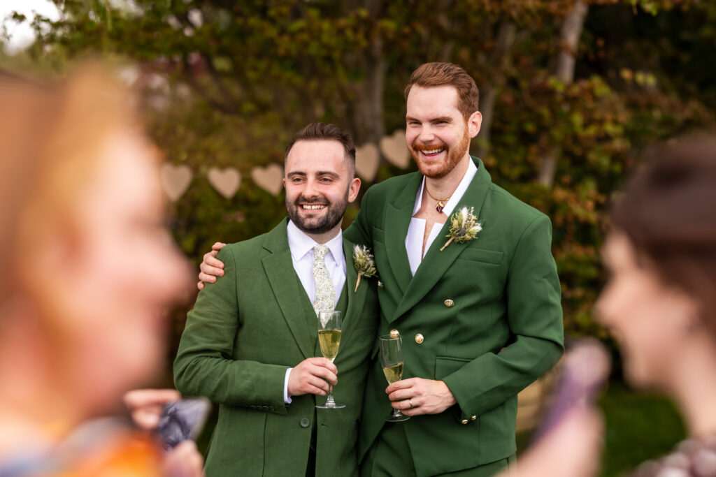 Two grooms in green suits holding champagne glasses