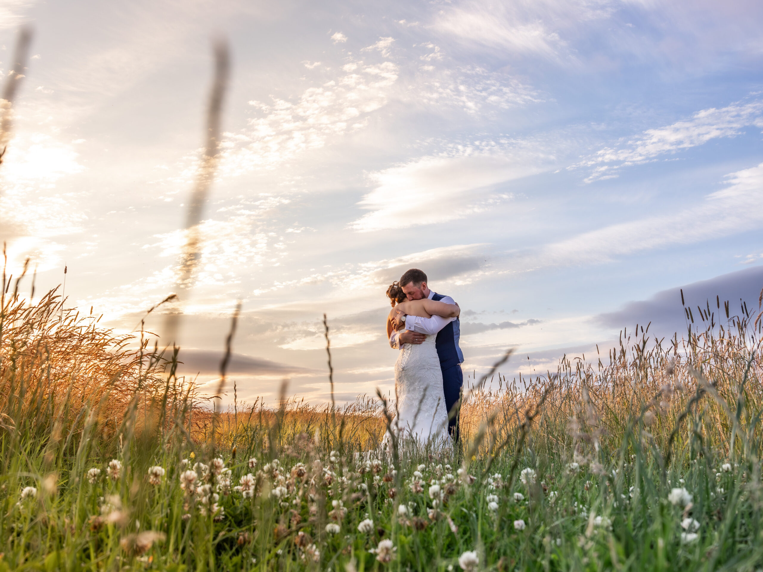 Newlyweds embrace in wildflower meadow at sunset